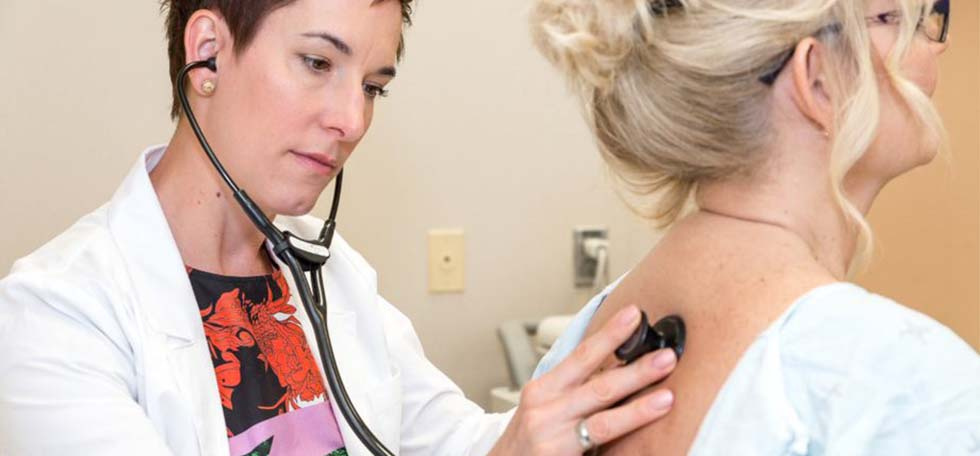 Doctor listening to woman breathe with stethoscope 